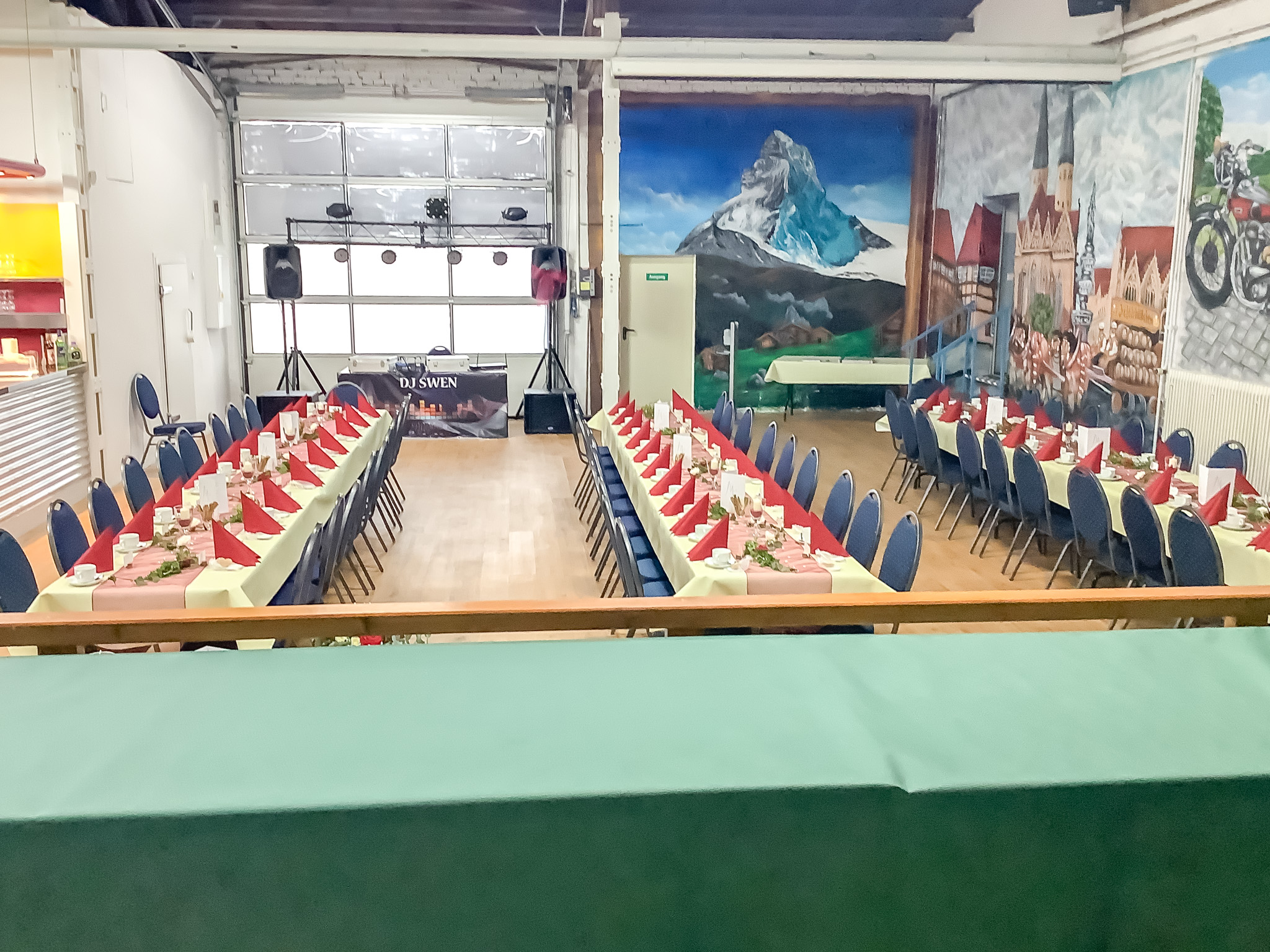 Großer Veranstaltungsraum mit farbenfrohen Wandmalereien und festlicher Tischdekoration für Events & Feiern.