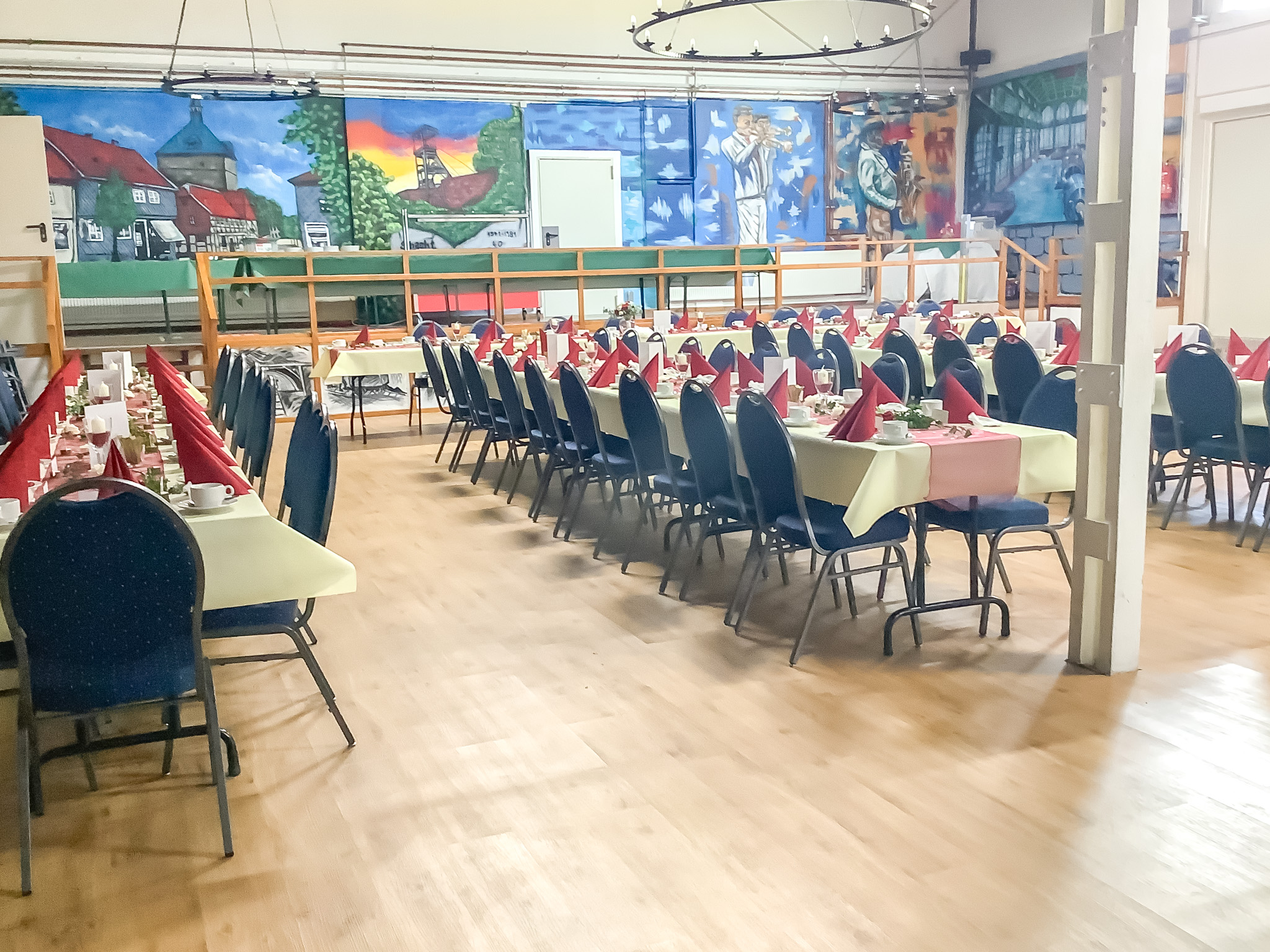Großer Veranstaltungsraum mit gedeckten Tafeln und farbenfroher Wandmalerei – ideal für Events und Feiern.